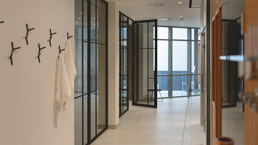 Mehrere schwarze Oslo-Wandhaken in modernem Design an einer weißen Wand im hellen Spa-Bereich des Hotels VierJahreszeiten in Iserlohn, an denen zwei weiße Handtücher hängen.