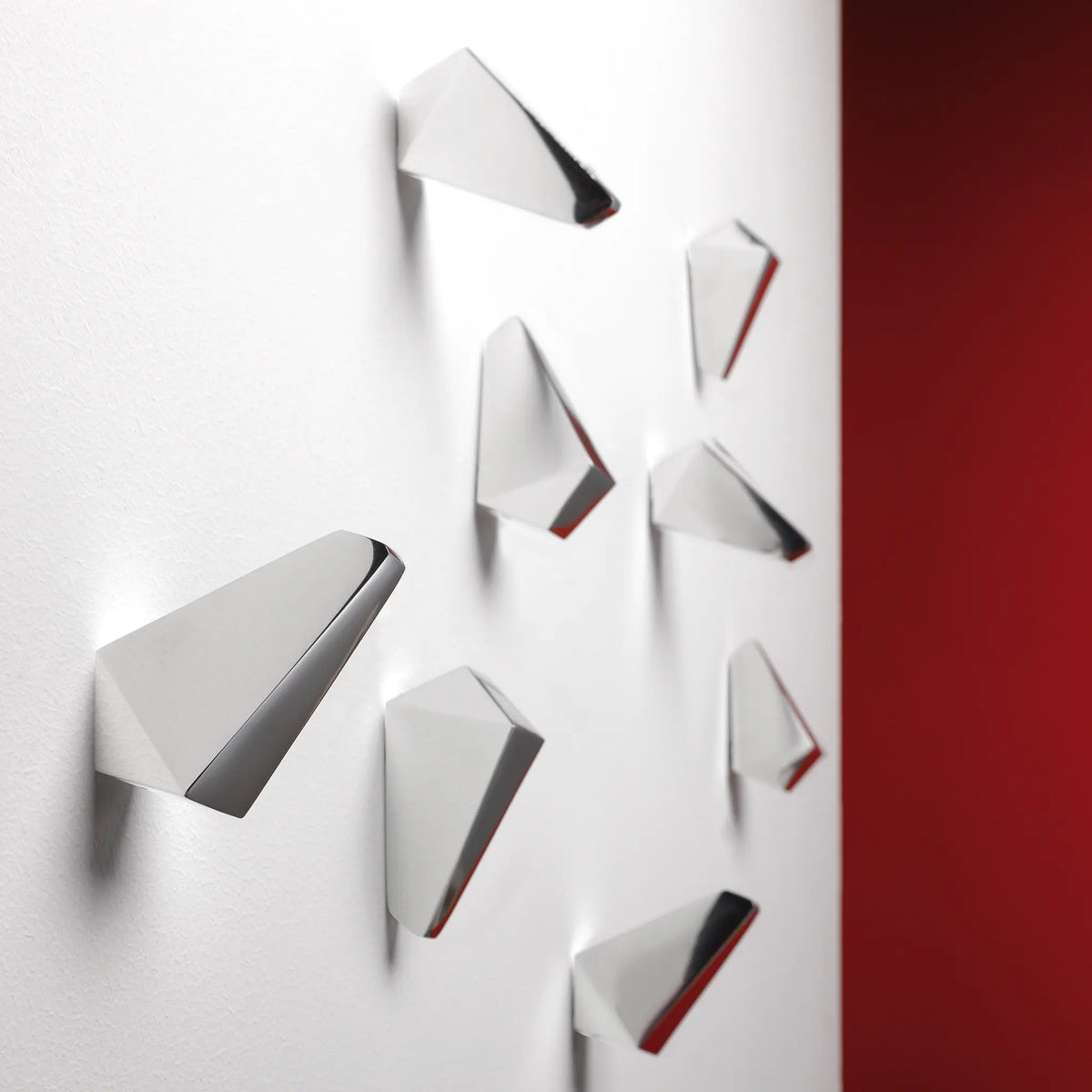 Geometrisch gefaltete INNY-Wandhaken an einer hellen Wand.