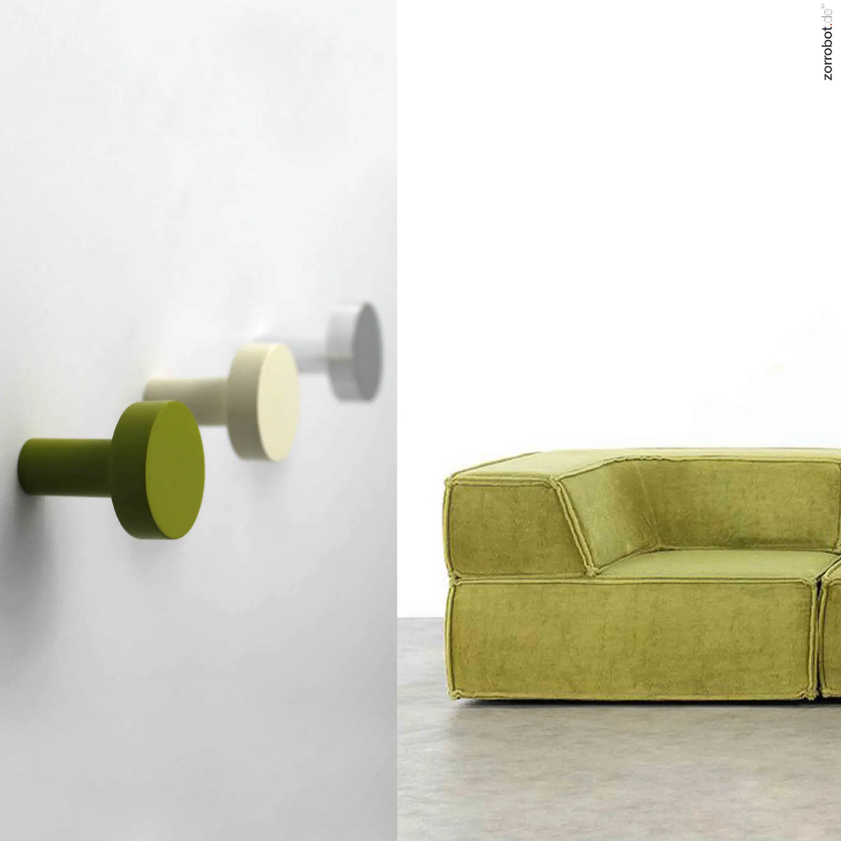 Scheibenhaken "Peking" in Olivgrün, Cremeweiß und Silber eloxiert an der Wand, daneben ein farblich passendes grünes Sofa.