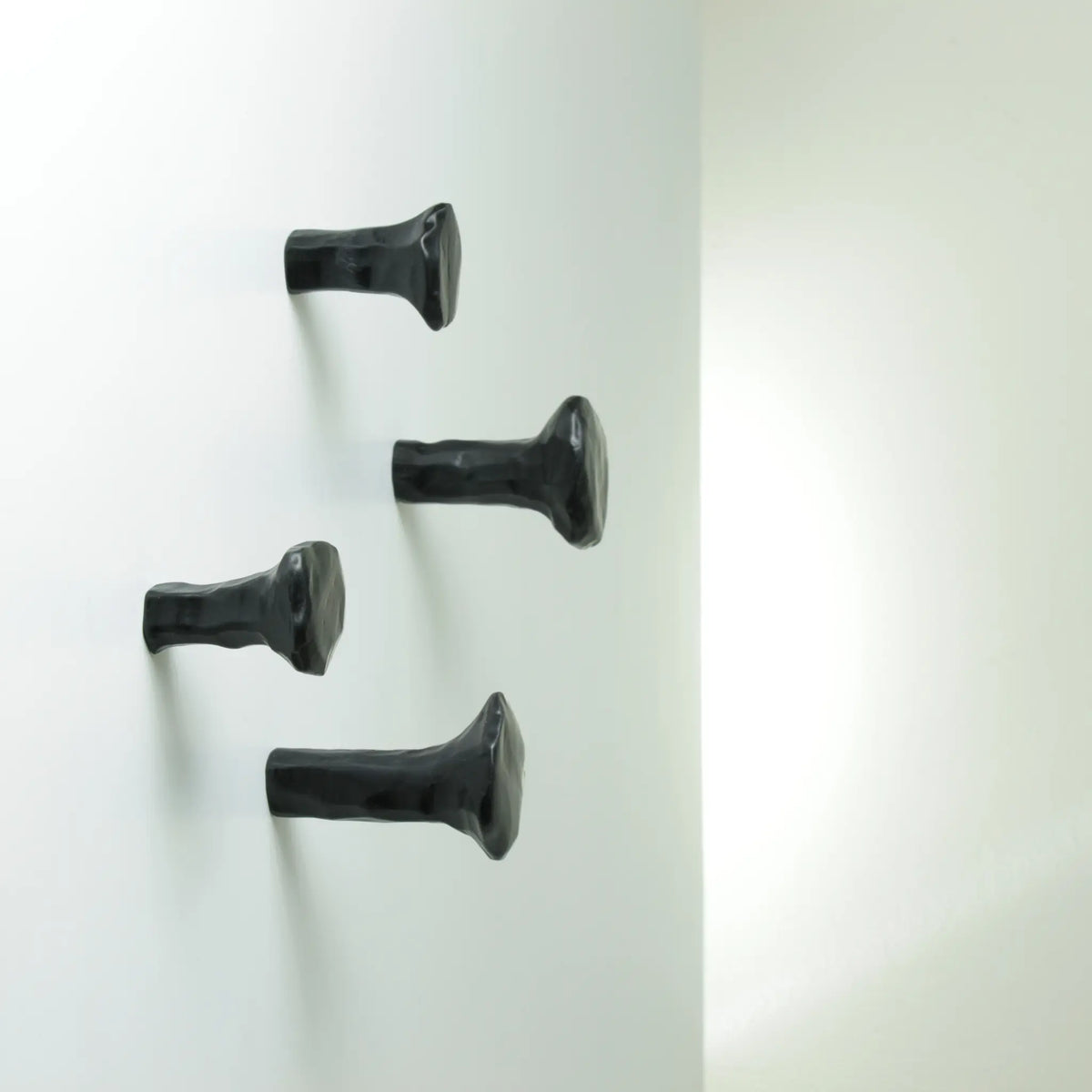 Vier schwarze SCHMIEDENAGEL-Stifthaken an einer hellen Wand.