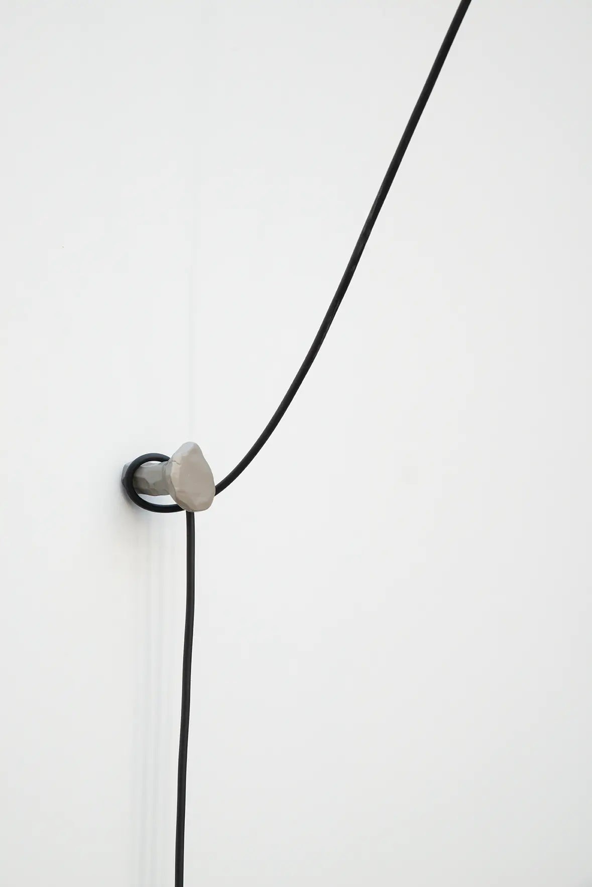 Detailaufnahme eines grauen Schmiedehakens an einer weißen Wand, über den ein langes, schwarzes Kabel geführt wird.